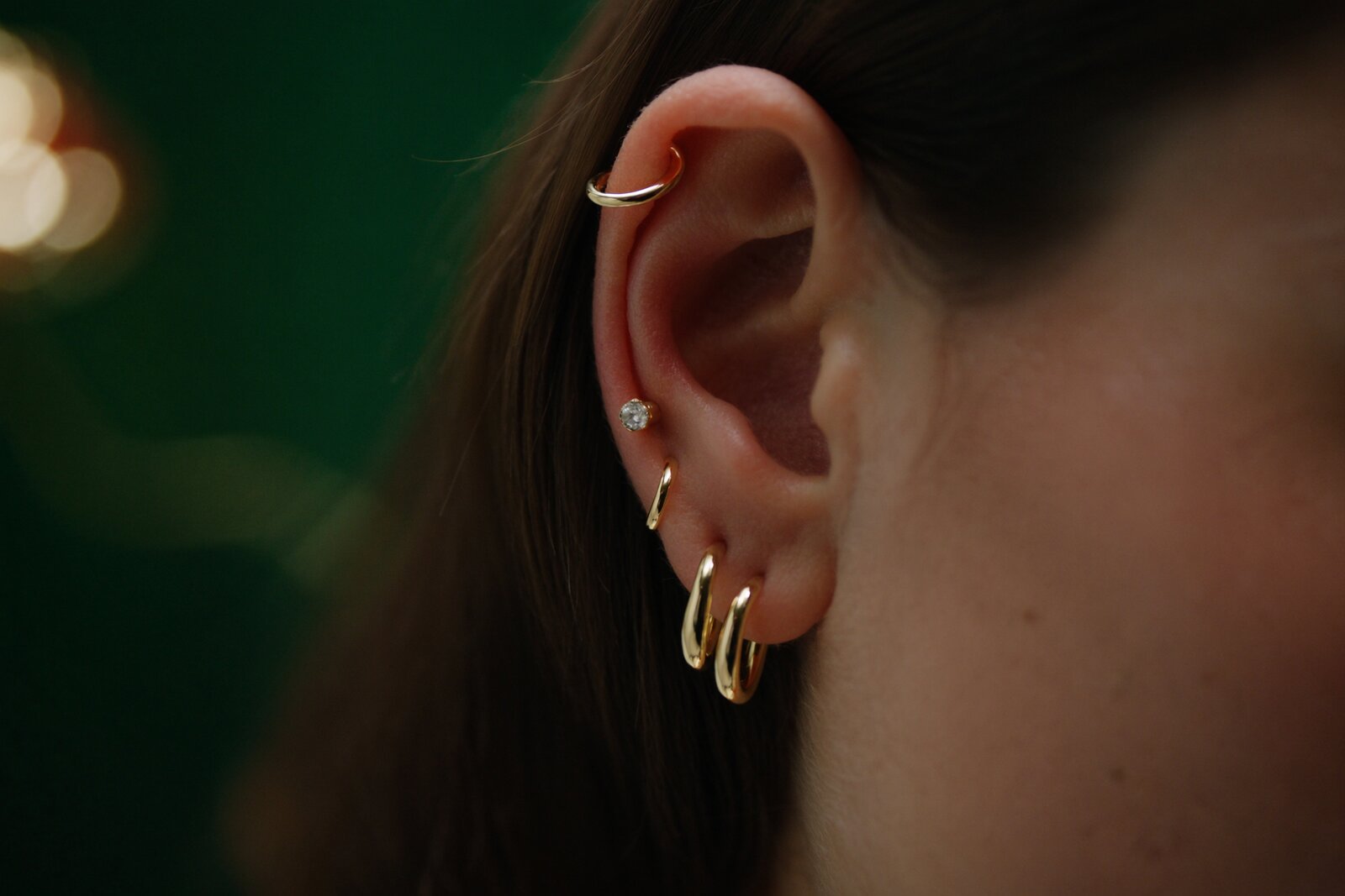 תקריב אוזן עם עיצוב Curated Ear — חישוק הליקס למעלה, נקב תנוך משובץ אבן וצמד חישוקי זהב — אריסטו פירסינג אשקלון